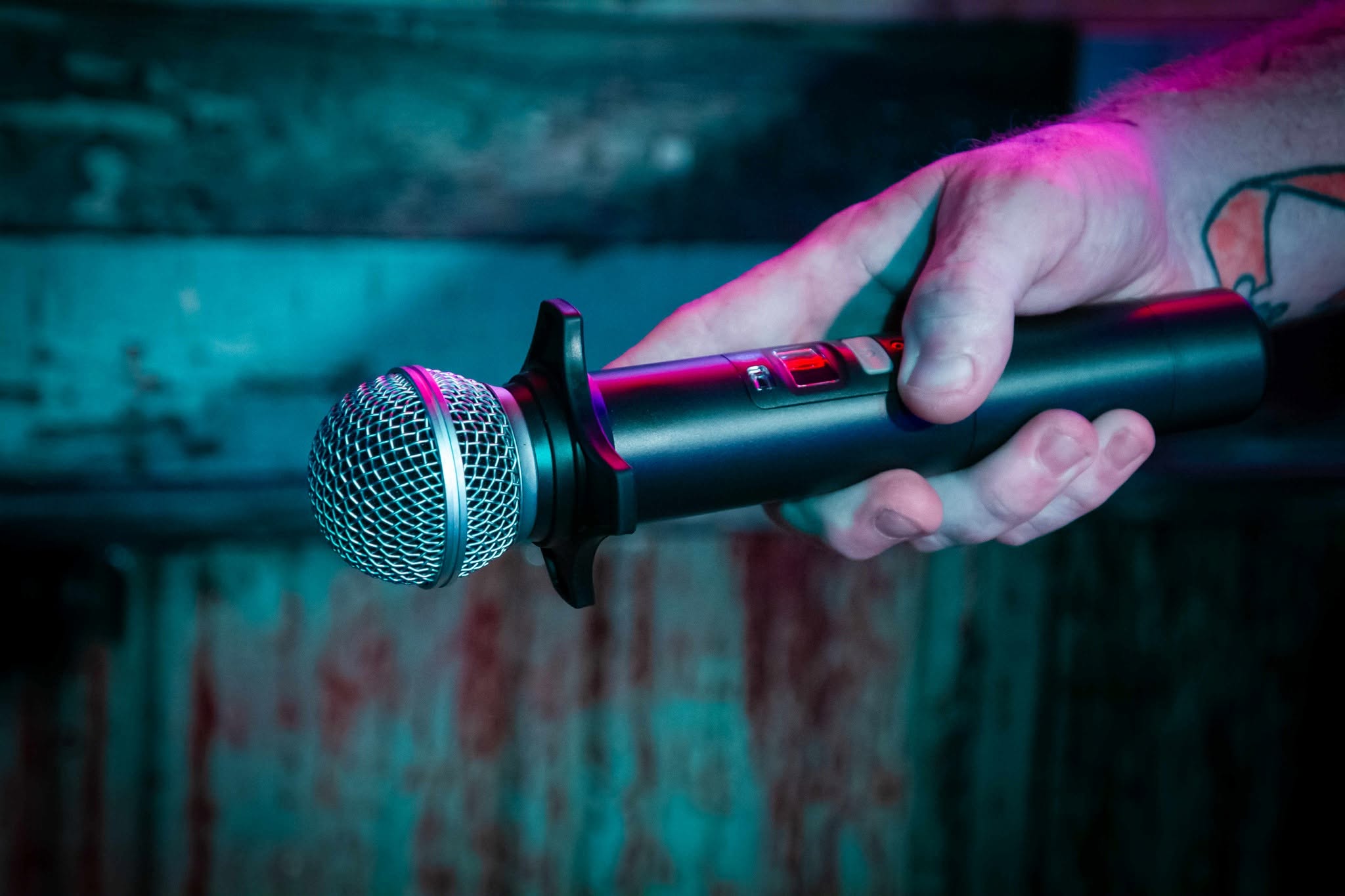 A hand holding a microphone under red and blue stage lighting